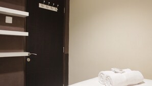 A hotel room with a dark wooden door, a white towel on the bed, and a towel rack with hooks on the wall. - Best Location 2BR Tamansari La Grande Apartment (Bandung)