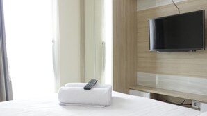 A hotel room with a bed, a remote control, and a television mounted on the wall. - Best Location 2BR Tamansari La Grande Apartment (Bandung)