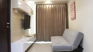 A modern living room with a sofa, a flat-screen TV, a wooden cabinet, and a window with curtains. - Best Location 2BR Tamansari La Grande Apartment (Bandung)