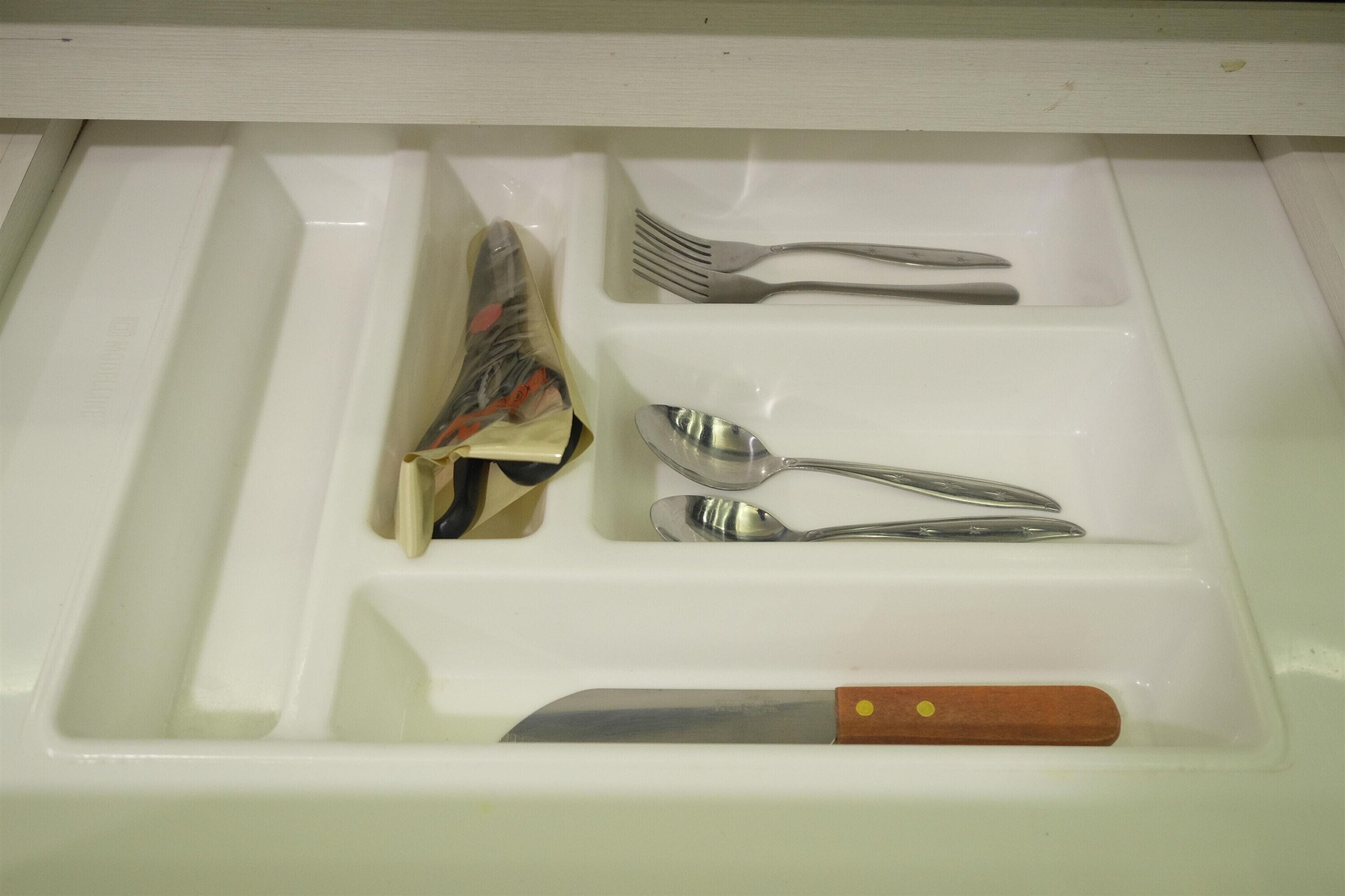 A drawer with utensils including a knife, fork, spoon, and a package.