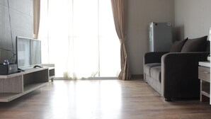 Ein modernes Wohnzimmer mit einem Flachbildfernseher auf einem Holzständer, einer Couch, einem kleinen Tisch und einem Kühlschrank.