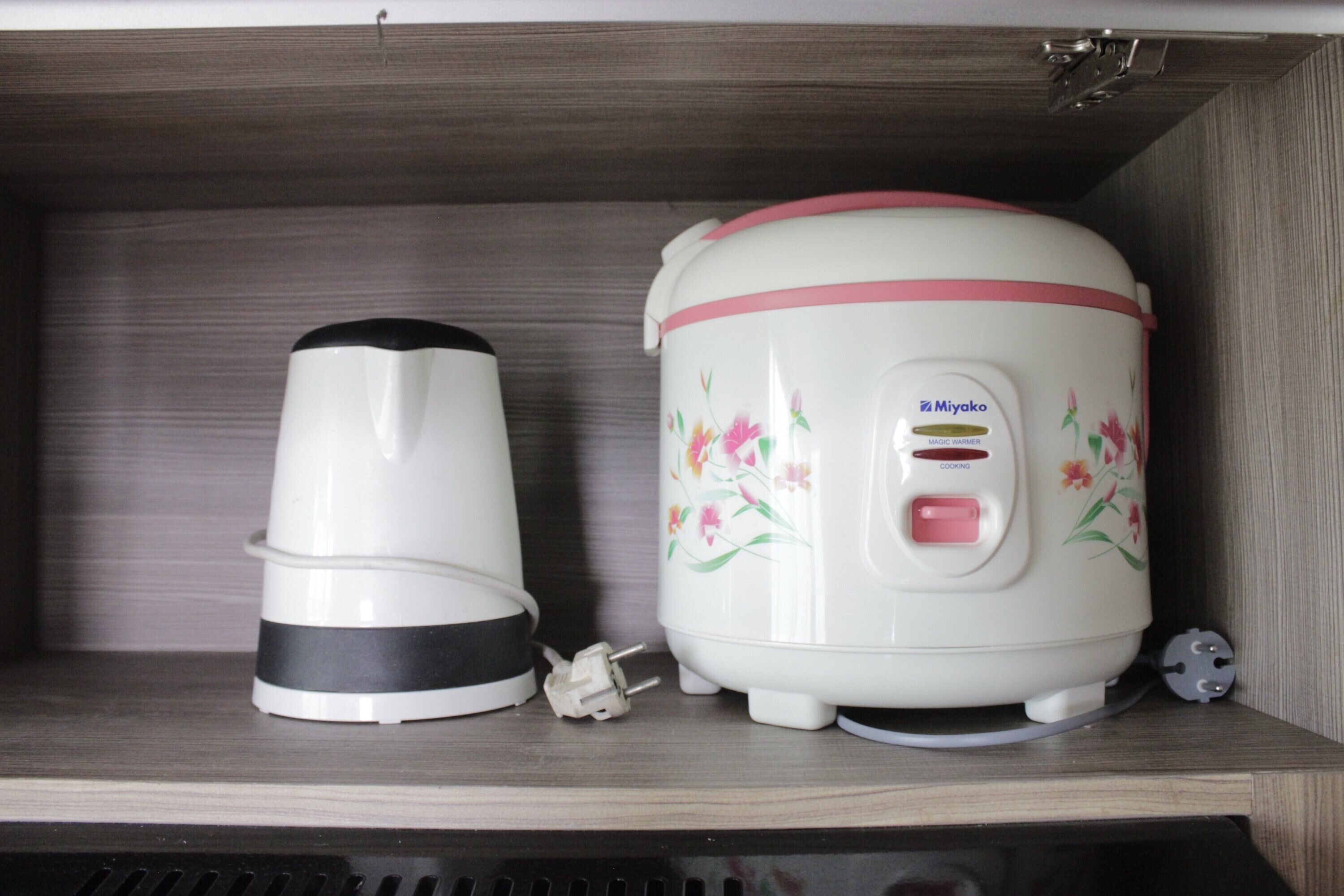 A kitchen shelf with a white electric kettle and a rice cooker with floral designs.