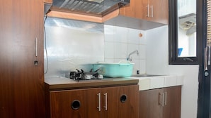 A kitchen with wooden cabinets, a stainless steel countertop, a sink, and a window with blinds. - Comfort and Homey Studio Kebagusan City Apartment (Jakarta)
