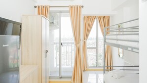 Une chambre d’hôtel avec une kitchenette, un lit avec un cadre en métal, une fenêtre avec des rideaux et une vue sur l’extérieur.