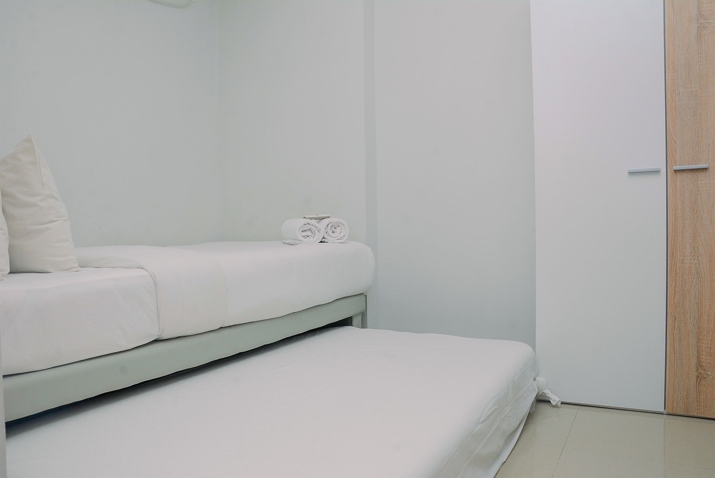 A small, white, single-bed room with a wooden door and a white wall.