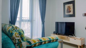 A living room with a sofa, a flat-screen TV, a small table, and a wall-mounted clock.