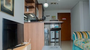 A compact living space with a TV, a small table, a sofa, and a kitchenette area.