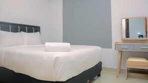 A neatly made bed with white linens and a folded towel, a wooden nightstand with a mirror, and a light-colored chair.