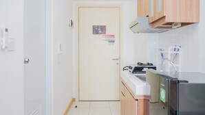 A small kitchen with a white door, a stove, a sink, and wooden cabinets. - Cozy Living Studio Apartment M-Town Residence (Gading Serpong)