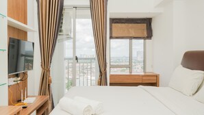 A hotel room with a bed, a TV, a desk, and a window with curtains. - Cozy Living Studio Apartment M-Town Residence (Gading Serpong)