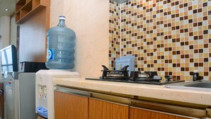 A kitchen with a water dispenser, a large water bottle, a microwave, and a tiled backsplash.