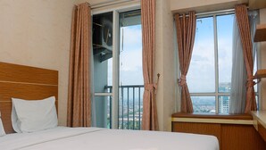 A hotel room with a large bed, a wooden headboard, a window with curtains, and a view of the cityscape.