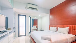A modern hotel room with a large bed, a TV, a bathroom with a glass shower, and a wooden accent wall. - Comfort Studio Tamansari Sudirman Apartment (Jakarta)