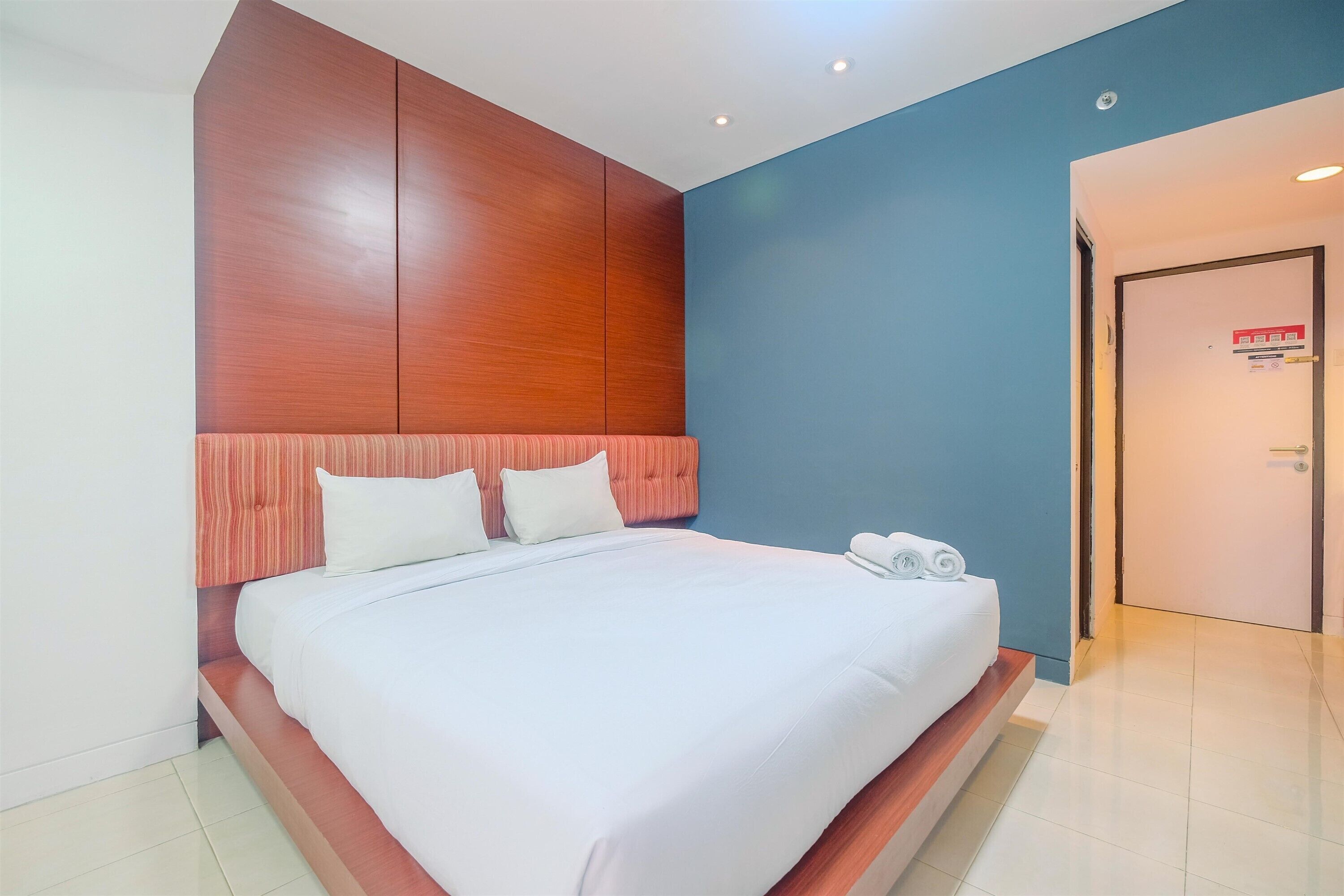 A hotel room with a large bed, wooden headboard, and a blue accent wall.