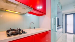 A modern kitchen with red cabinets, a stainless steel stove, and a sink. - Comfort Studio Tamansari Sudirman Apartment (Jakarta)