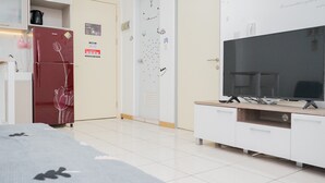 A modern hotel room with a large flat-screen TV, a white wardrobe, and a red refrigerator. - Comfort and Spacious 2BR Apartment M-Town Residence (Gading Serpong)