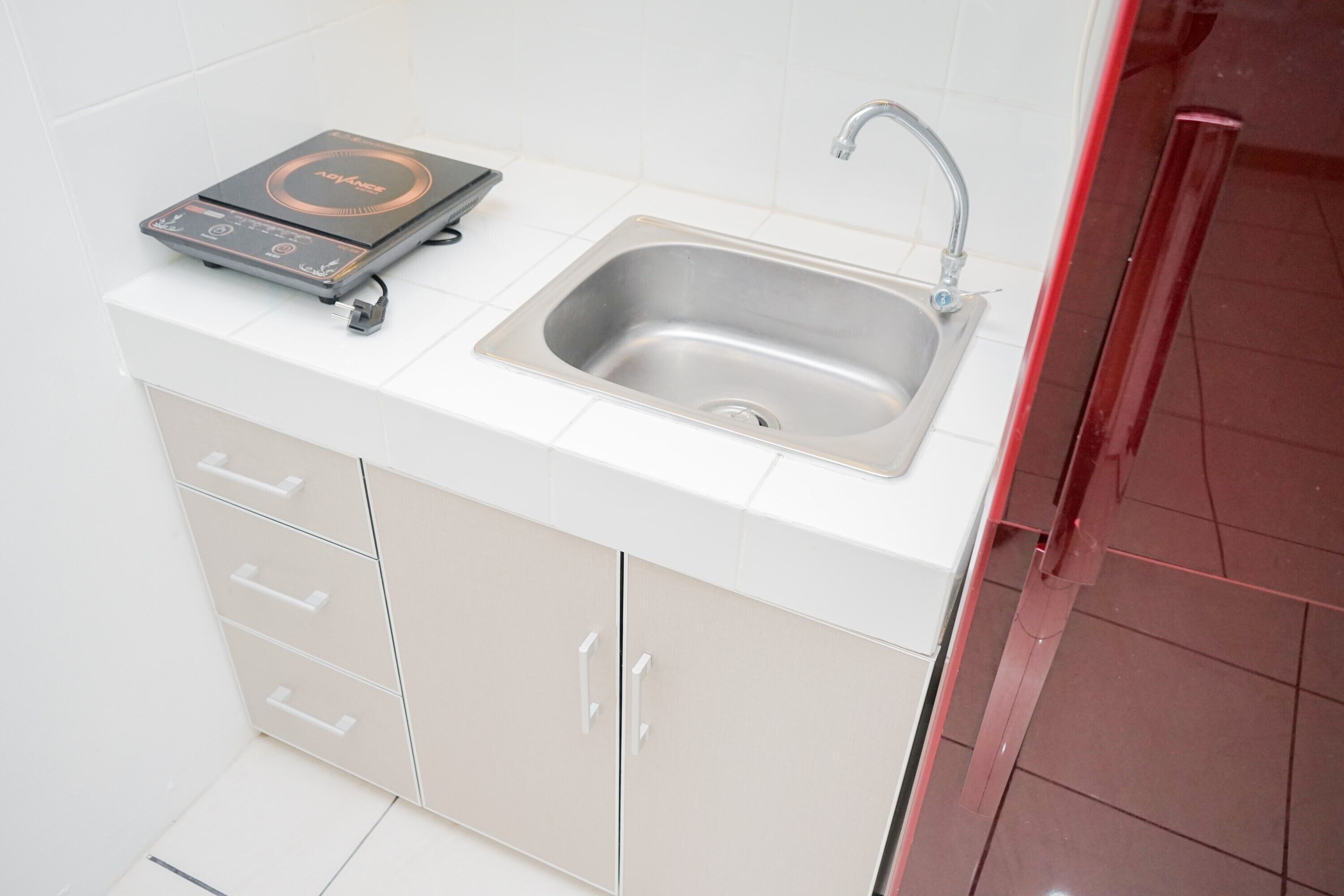 A kitchen with a stainless steel sink, a built-in induction cooktop, and a white tiled backsplash.