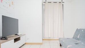 A bedroom with a TV on a wooden stand, a bed with a patterned blanket, and a curtain. - Comfort and Spacious 2BR Apartment M-Town Residence (Gading Serpong)