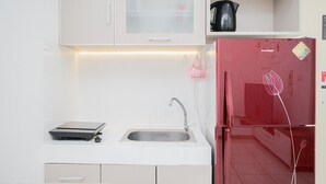 A kitchen with white cabinets, a stainless steel sink, a red refrigerator, and a kettle on the countertop. - Comfort and Spacious 2BR Apartment M-Town Residence (Gading Serpong)