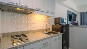 A modern kitchen with white cabinets, a gas stove, a sink, and a refrigerator. - Brand New Studio Apartment at H Residence (Jakarta)
