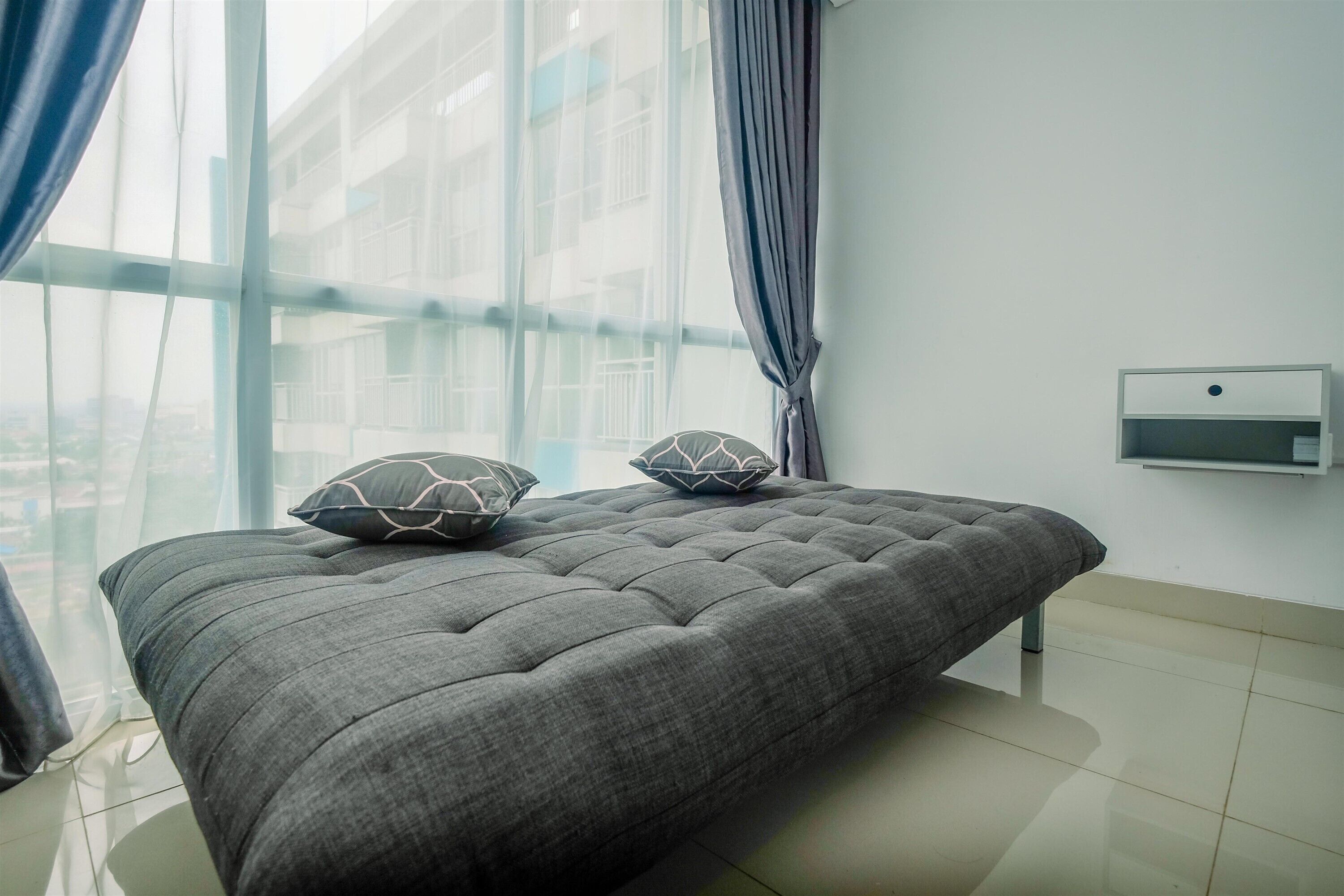 A modern bedroom with a large bed, a window with curtains, and a small bedside table.
