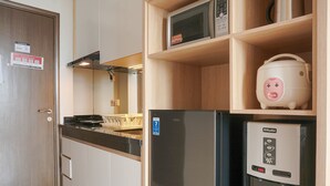Cocina pequeña con nevera, microondas y cocedor de arroz sobre estantes.