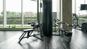 Un gimnasio con equipo de ejercicio, ventanas amplias y vistas al exterior con vegetación.