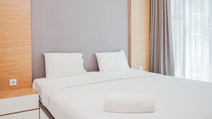 A neatly made bed with white linens, a grey headboard, and a window with curtains. - Great Choice 1BR at Brooklyn Alam Sutera Apartment (South Tangerang)