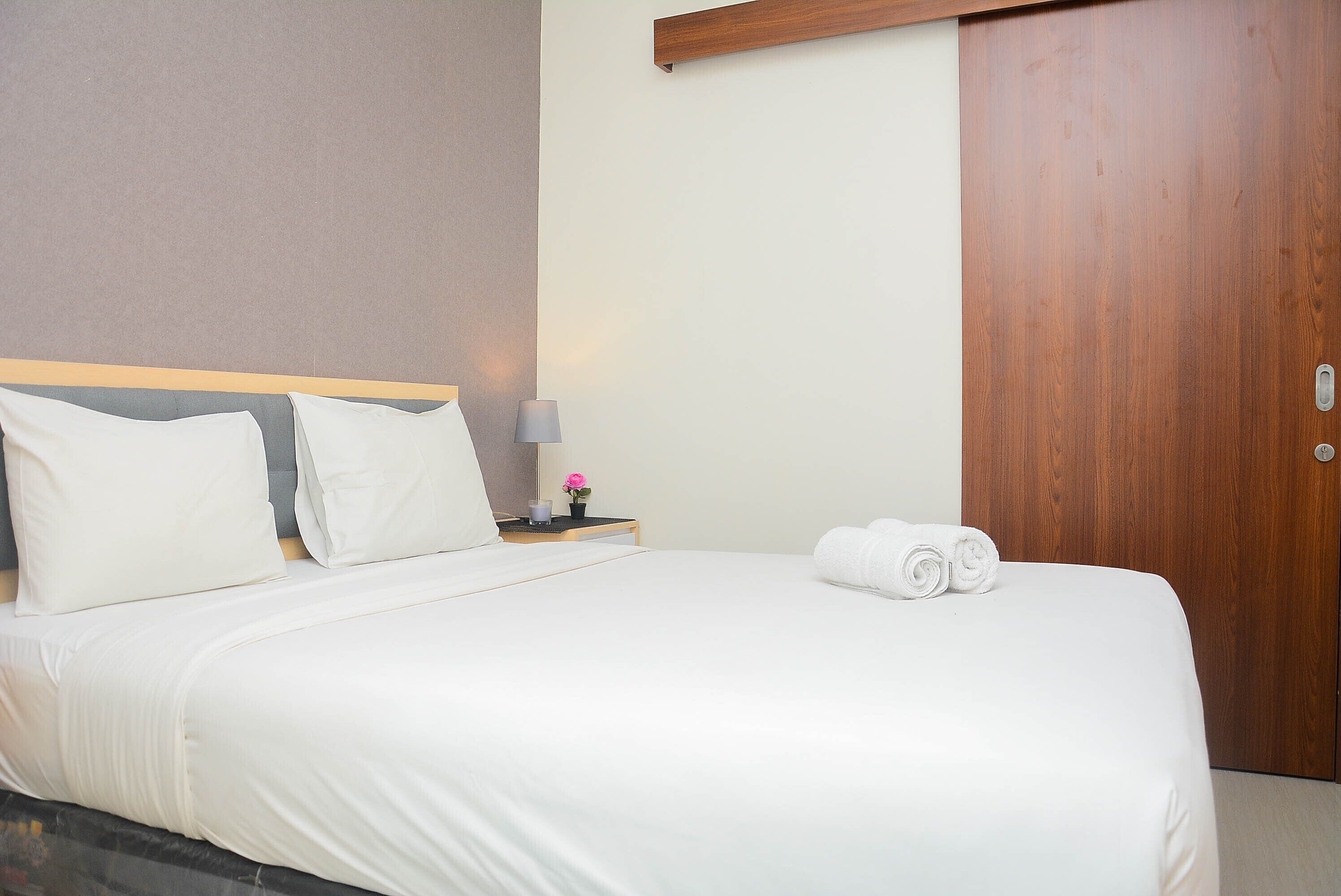 A neatly made bed with white linens, a wooden headboard, a nightstand with a lamp, and a wooden door.