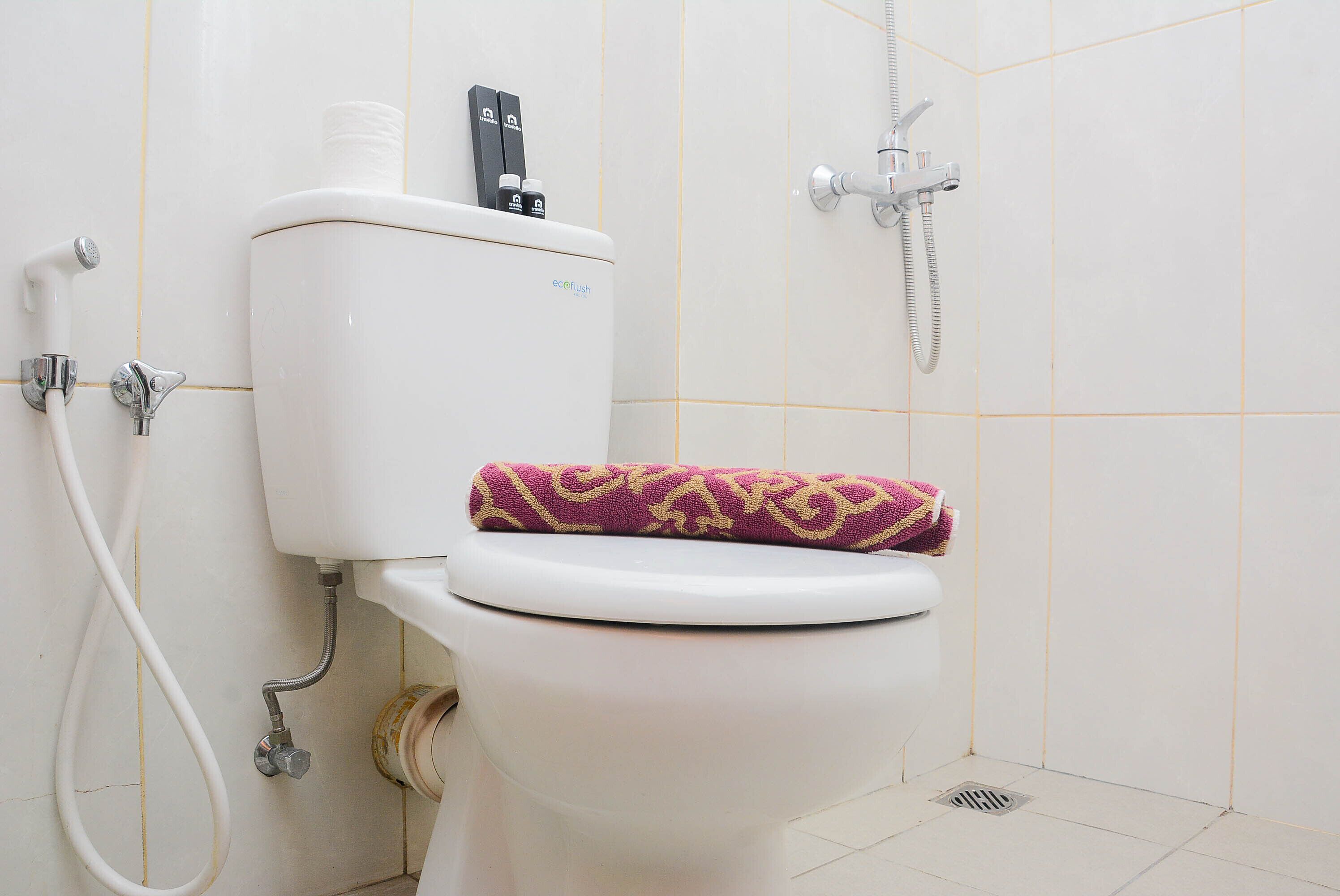 A toilet with a patterned seat cover, a toilet paper holder, and a bidet attachment.