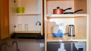 A compact kitchen with a Samsung refrigerator, a coffee maker, a kettle, and a frying pan on the countertop. - Cozy Stay 1BR at Grand Kamala Lagoon Apartment (Bekasi)