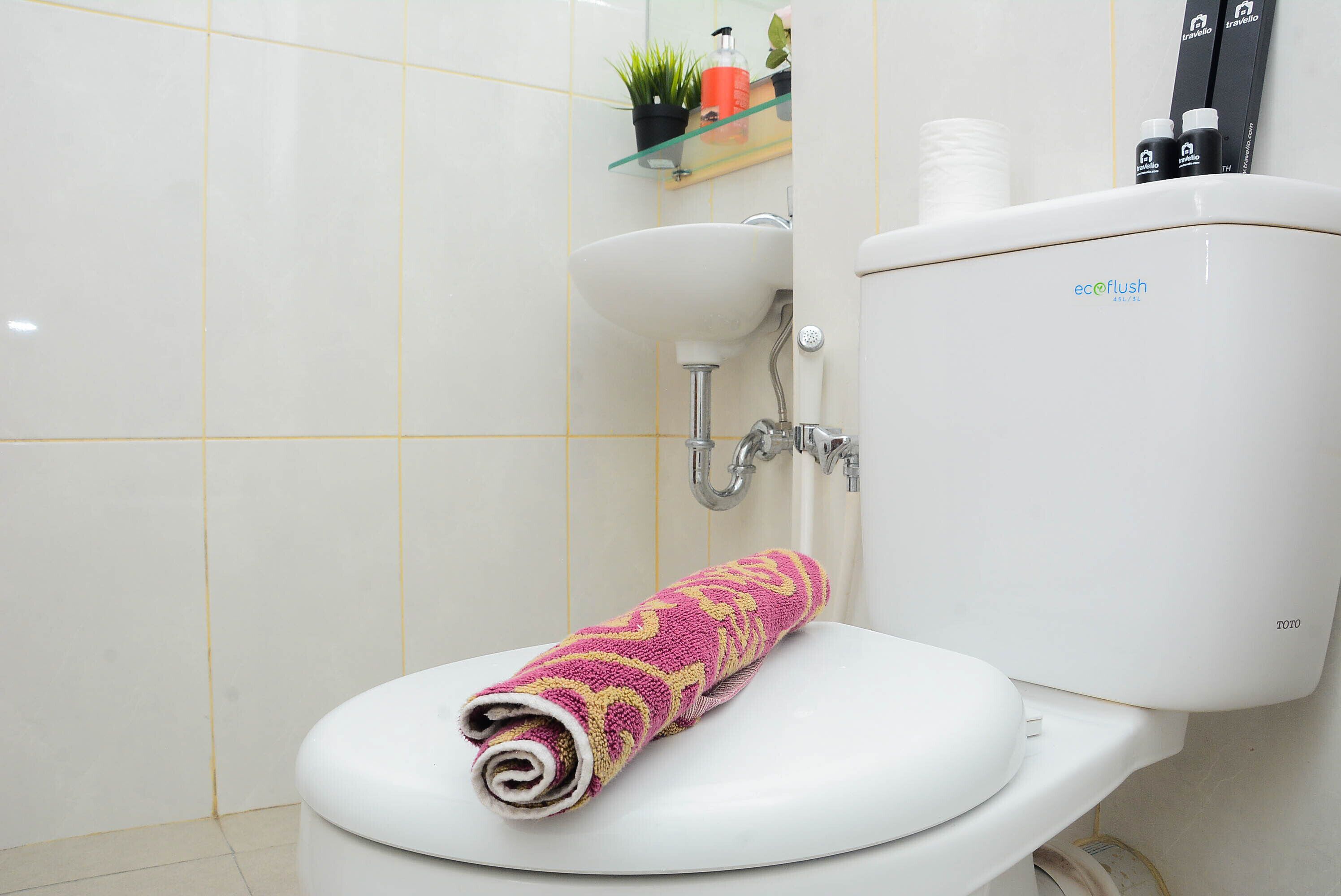 A bathroom with a white toilet, a glass shelf with toiletries, and a white sink.