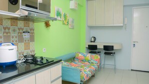 A compact kitchen with a gas stove, a microwave, and a sink. There is a small dining area with a table and chairs. The walls are painted green, and there are decorative wall hangings. - Comfortable 2BR Bassura City Apartment near Bassura Mall (Jakarta)