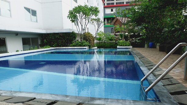 A rectangular swimming pool with a metal ladder on one side, surrounded by a pebble border. - Comfortable 2BR Bassura City Apartment near Bassura Mall (Jakarta)