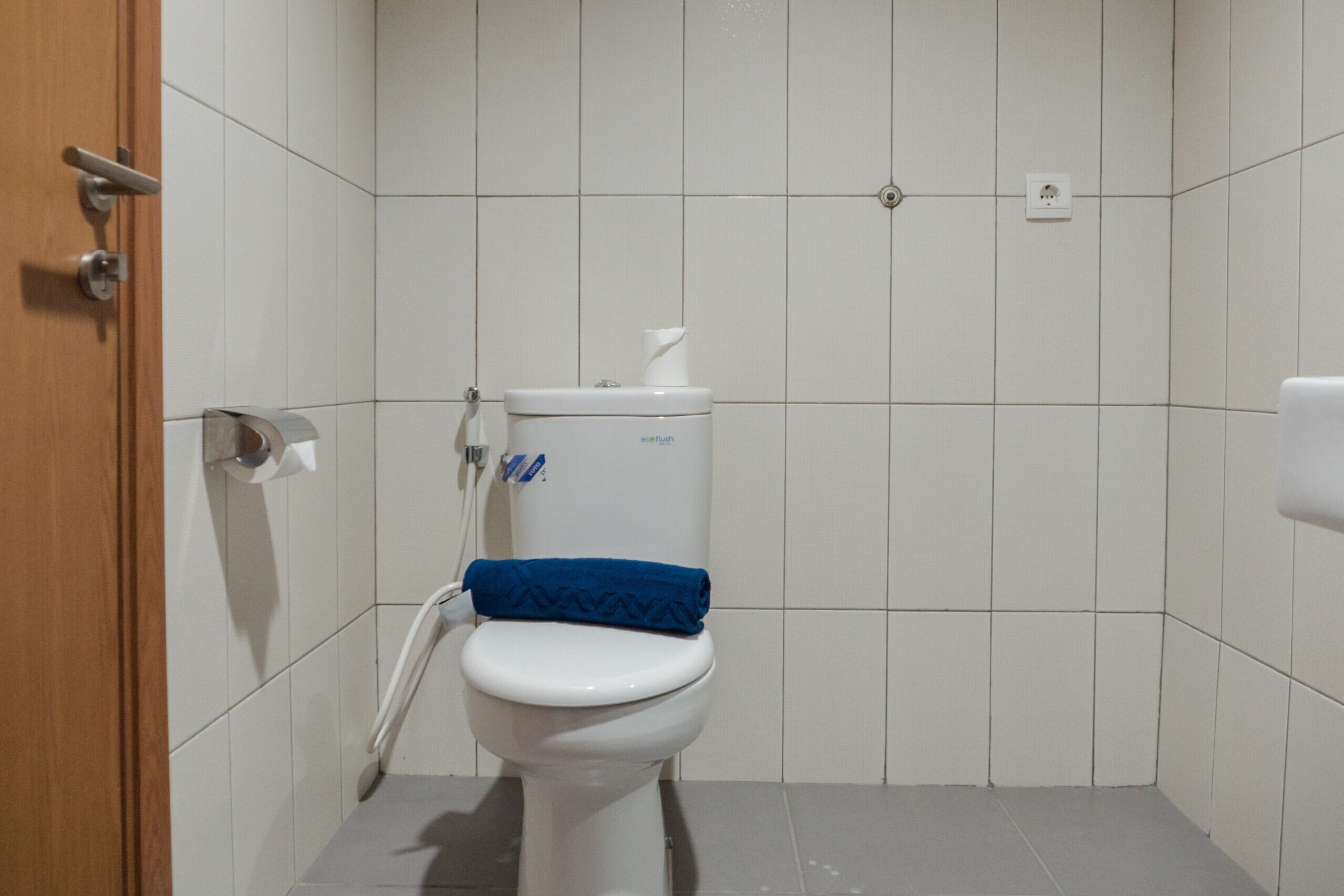 Et lille, rent badeværelse med toilet, papirhåndklædedispenser og hårtørrer.