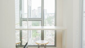 A room with a large window overlooking a cityscape. There is a small table and a chair in the foreground. - Great Choice Studio Apartment M-Town Residence near Summarecon Mall (Gading Serpong)