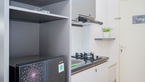 A compact kitchen with a gas stove, a black refrigerator, and a small potted plant on a shelf. - Great Choice Studio Apartment M-Town Residence near Summarecon Mall (Gading Serpong)
