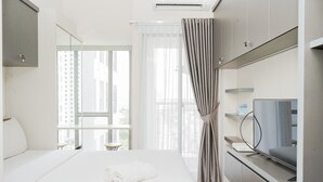 A modern hotel room with a large bed, a TV, and a view of the city through the window. - Great Choice Studio Apartment M-Town Residence near Summarecon Mall (Gading Serpong)