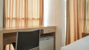 Una camera d'albergo con una scrivania in legno, una sedia, un piccolo frigorifero e un letto.