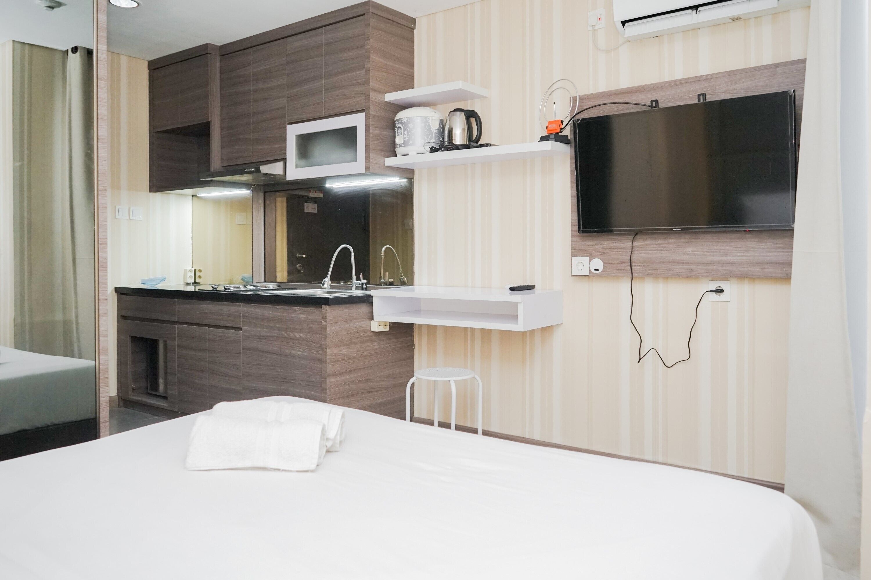 A modern hotel room with a bed, a small kitchenette, a TV, and a window with curtains.