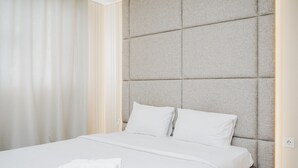 A neatly made bed with white linens and pillows, a folded white towel on the bed, and a textured headboard. - Modern Classic Studio Room Bintaro Icon Apartment (South Tangerang)