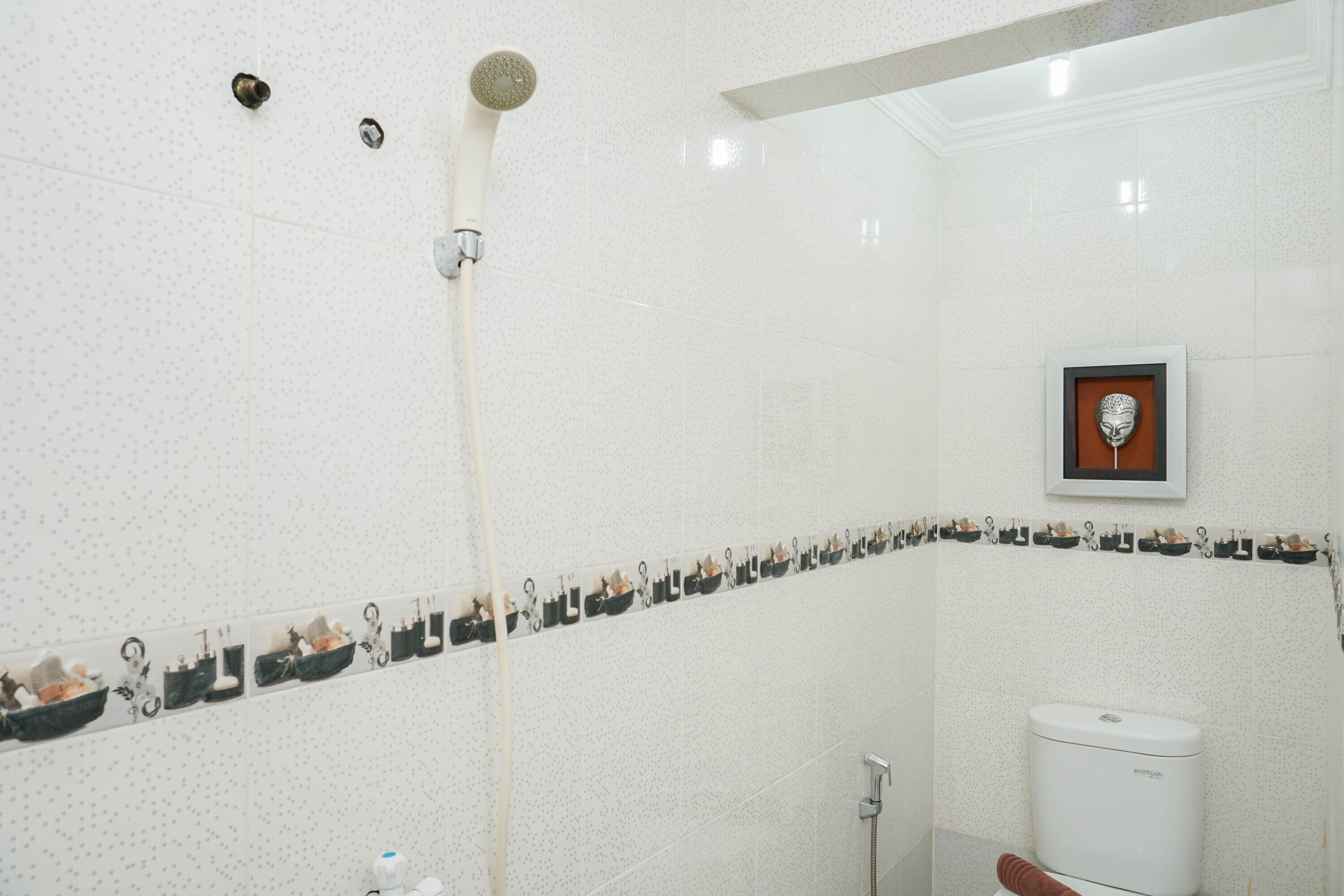 A bathroom with a shower, toilet, and a decorative wall with a framed picture.