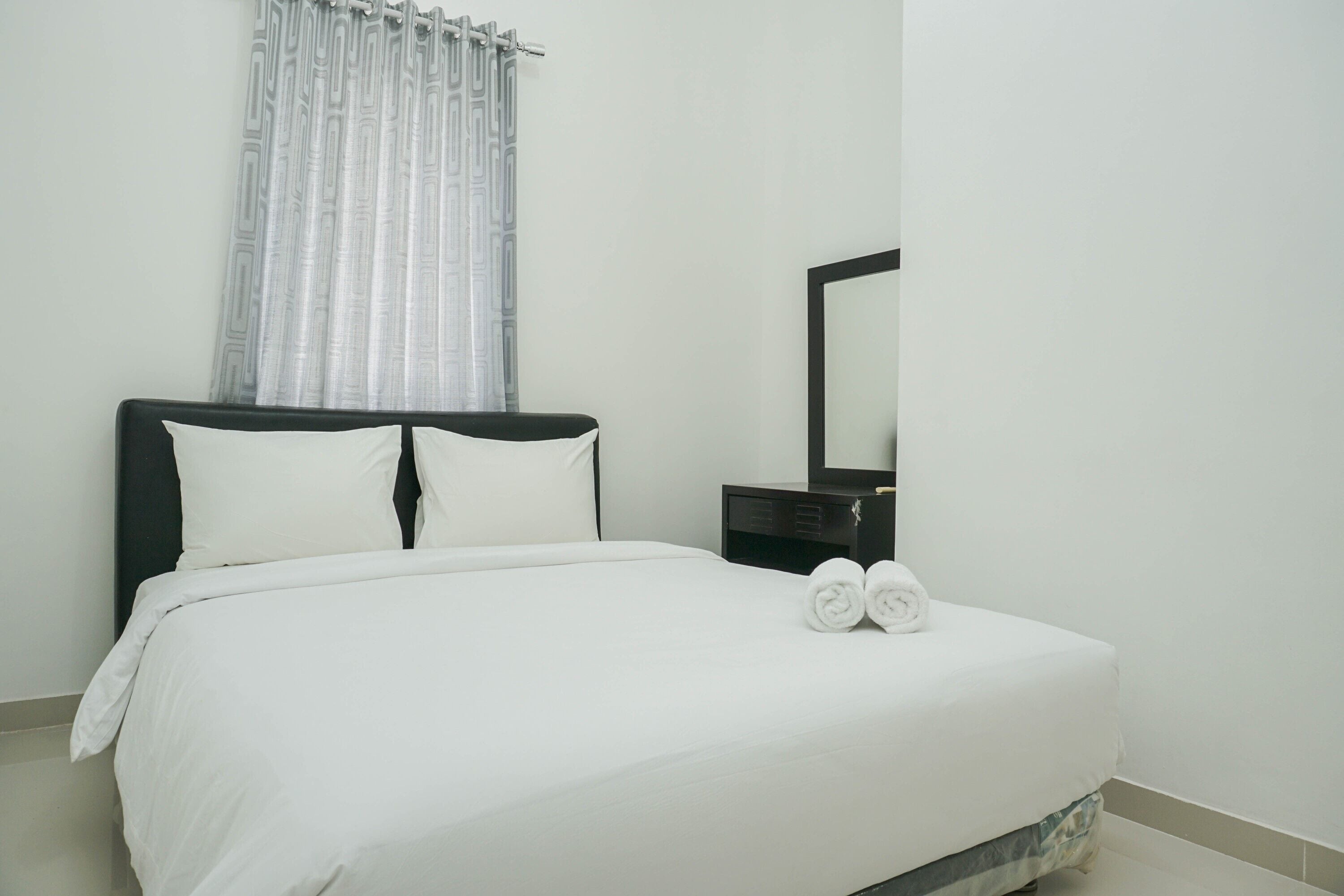 A neatly made bed with white linens, a black headboard, and two rolled towels on the foot of the bed.