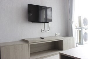 Una sala de estar moderna con un televisor de pantalla plana montado, un mueble de entretenimiento de madera y un amplio ventanal, donde se observa una unidad de aire acondicionado en el exterior.