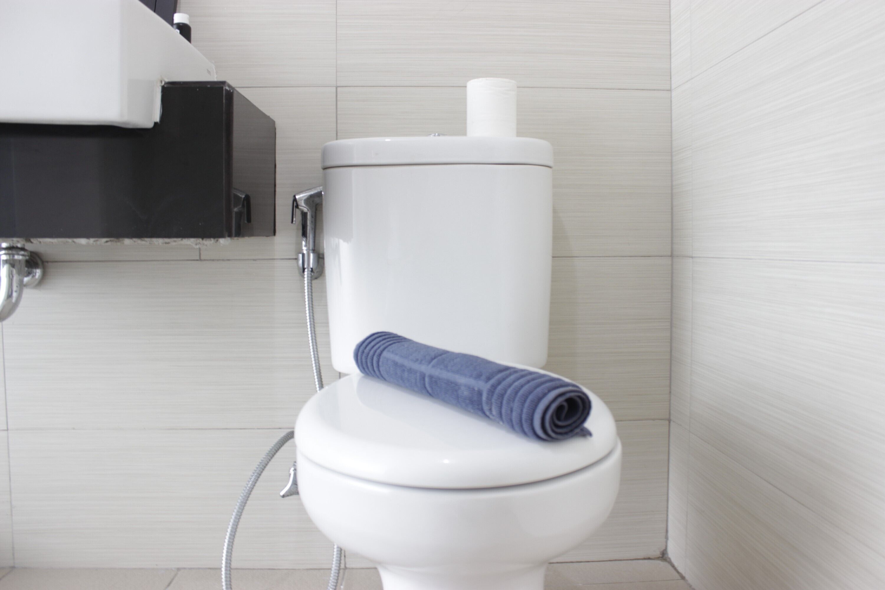 A white toilet with a towel on top, a toilet paper holder, and a showerhead.