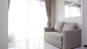 A minimalist living room with a neutral-colored sofa, a large window with sheer curtains, and a mirror on the wall.