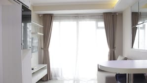 A modern hotel room with a white dining table, a sofa, and a TV on a stand.
