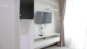 A modern living room with a flat-screen TV mounted on a white wall, a built-in shelf below, and a power outlet.