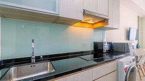 A modern kitchen with a stainless steel sink, black countertop, and a built-in washing machine. - Warm and Cozy Studio Room at Menteng Park Apartment (Jakarta)