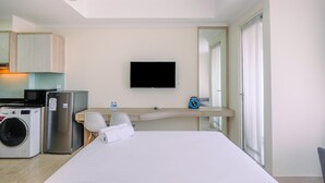 A hotel room with a bed, a TV, a washing machine, a refrigerator, a microwave, a small table with a chair, and a window with curtains. - Warm and Cozy Studio Room at Menteng Park Apartment (Jakarta)